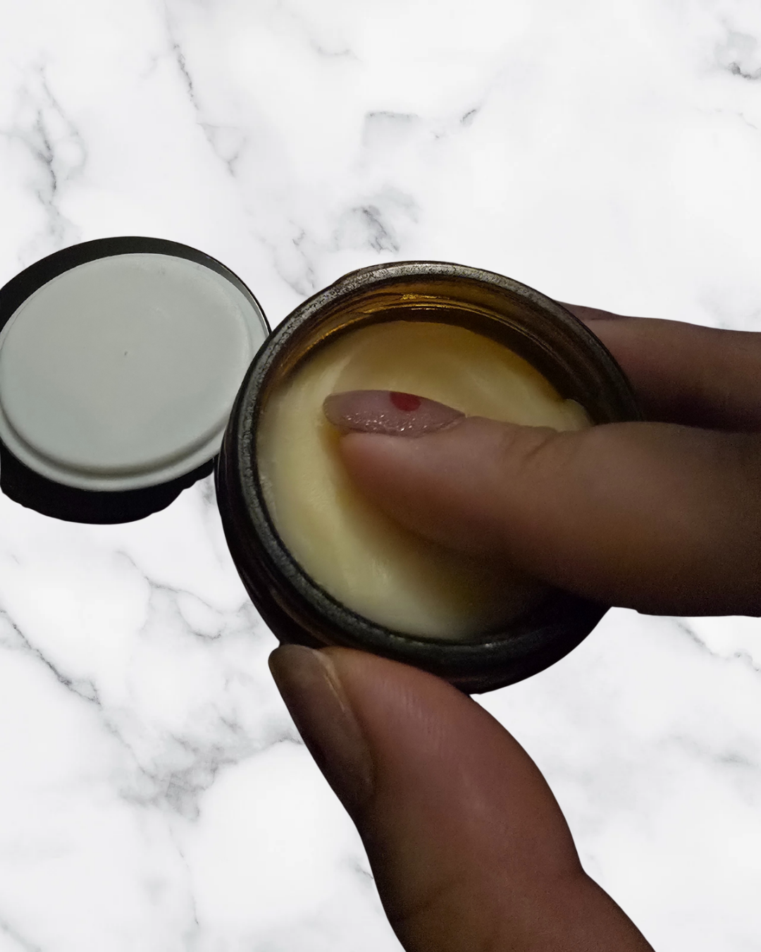 Hand holding a jar of cream with a marble background